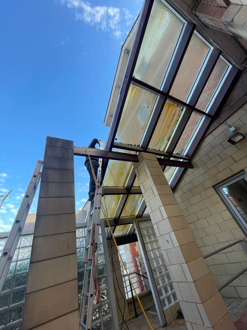 Before: worker on an extension ladder starting to clean a glass canopy