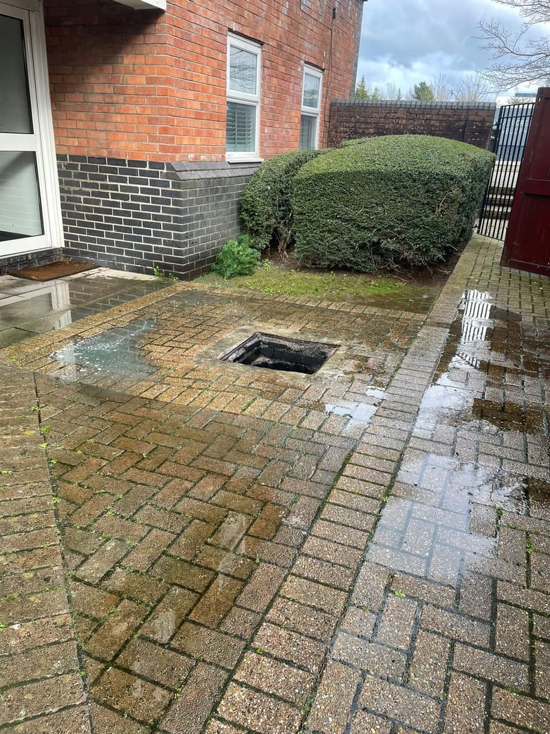 Open manhole on a wet brick driveway during drain jetting