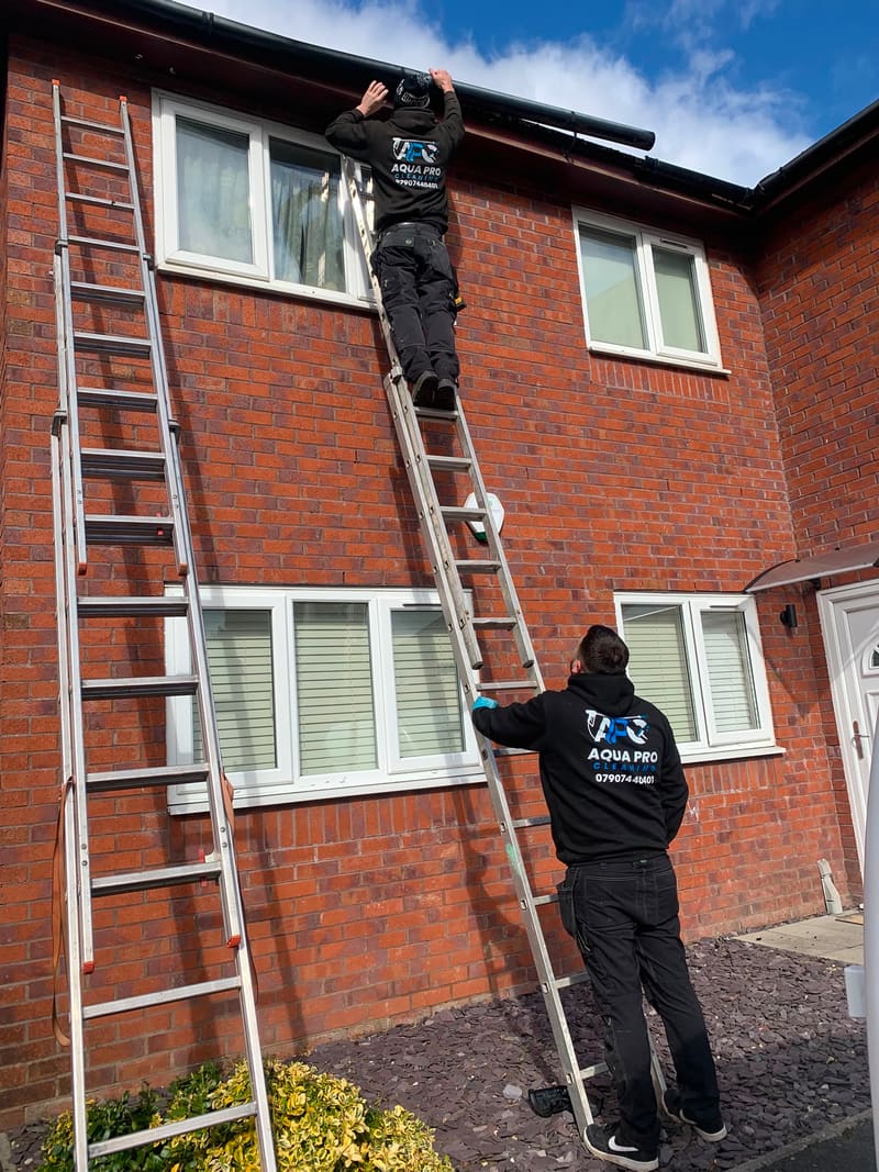 Aqua Pro Cleaning technicians cleaning gutters on a brick home