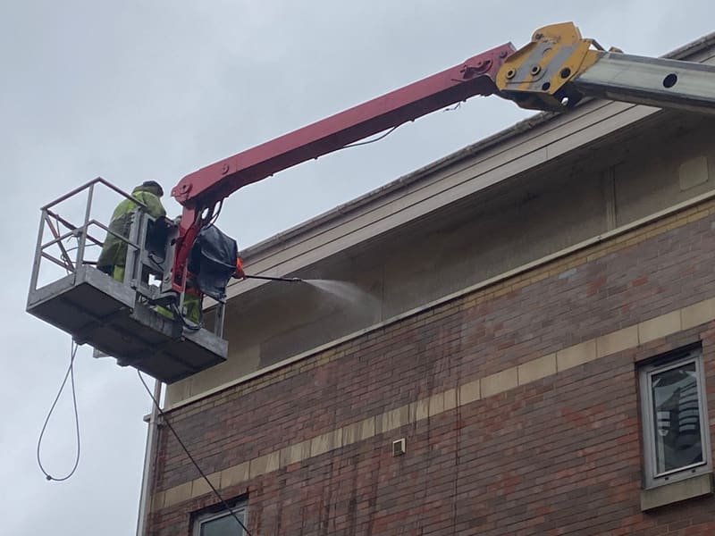 Worker pressure washing a building from a cherry picker