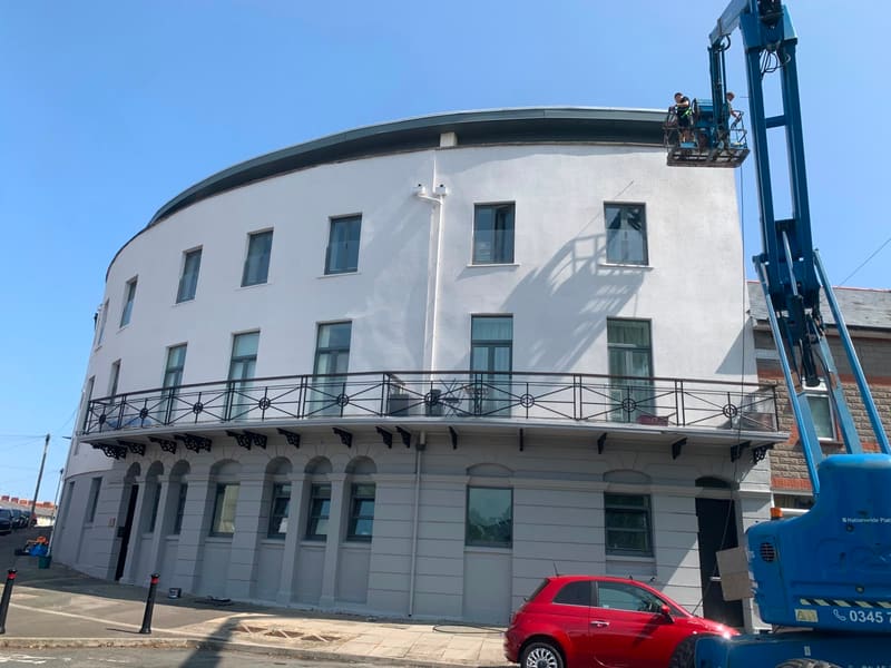 Workers on a cherry picker painting a curved white building