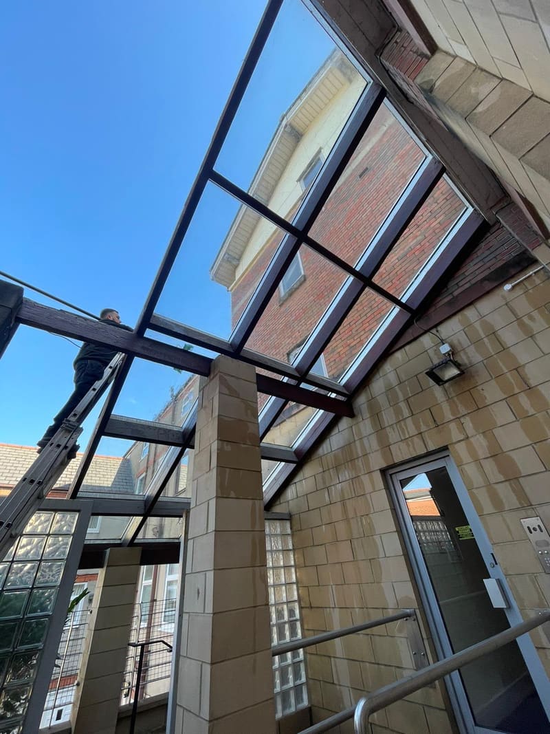 Worker cleaning glass roof panels from a ladder